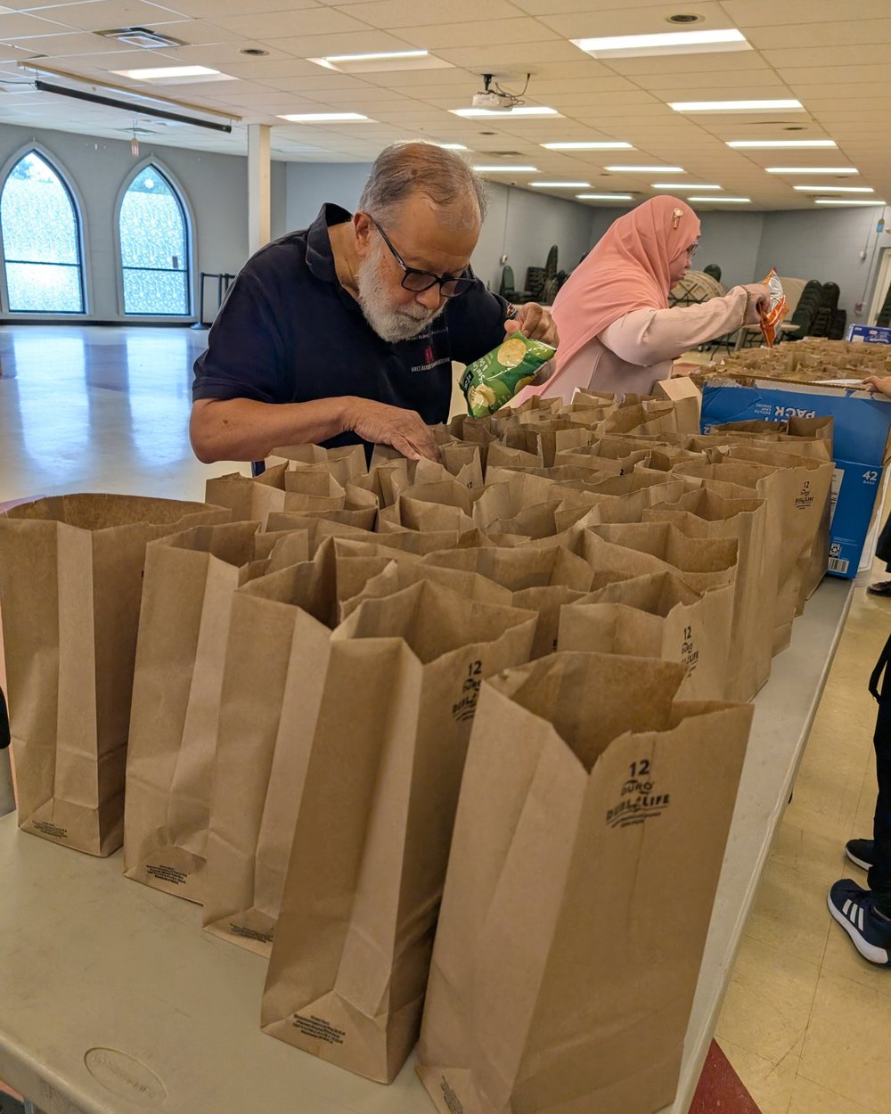 An older volunteer filling brown lunch bags with chips