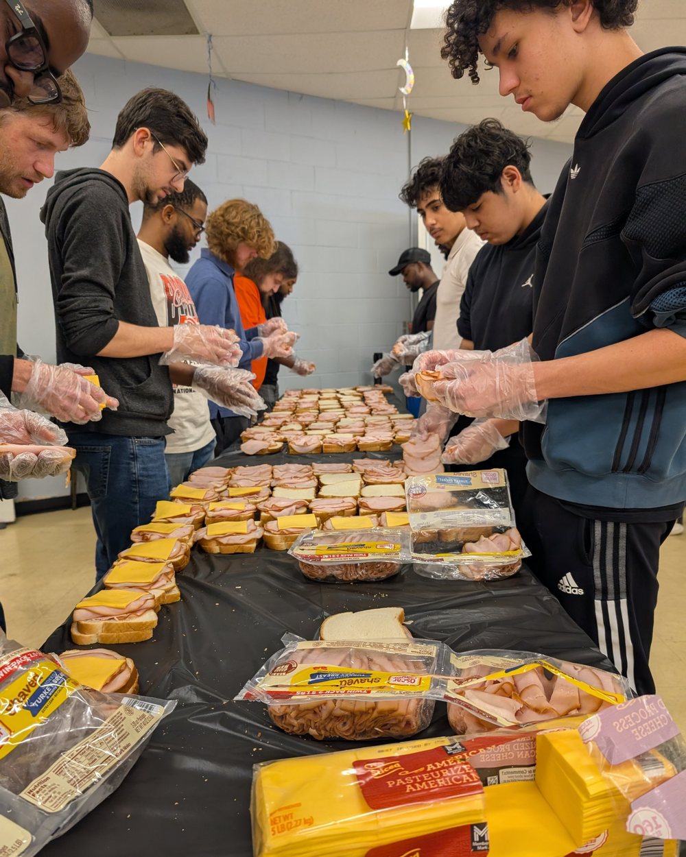 A line of volunteers in gloves assembling turkey and cheese sandwiches